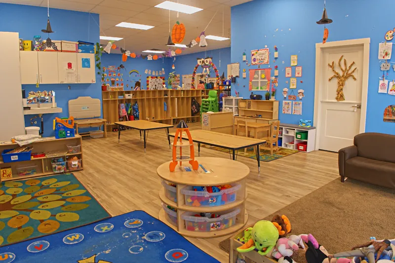 Blue classroom with a round toy shelf, soft rugs and a cosy couch