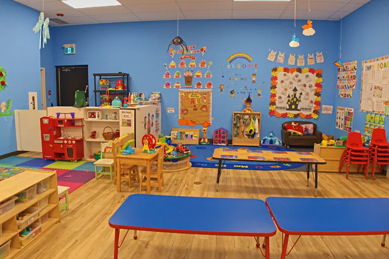 Blue classroom with a play kitchen, reading rug and low tables