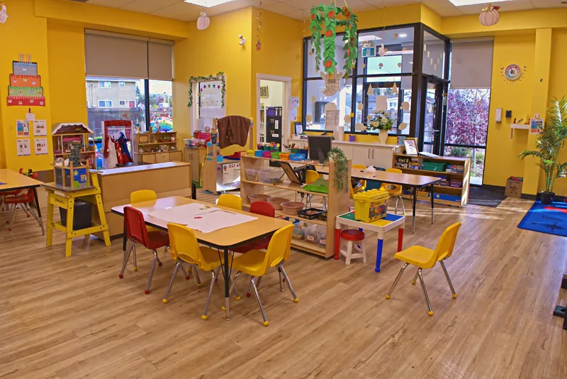 Sunny yellow classroom with small tables, chairs and art supplies