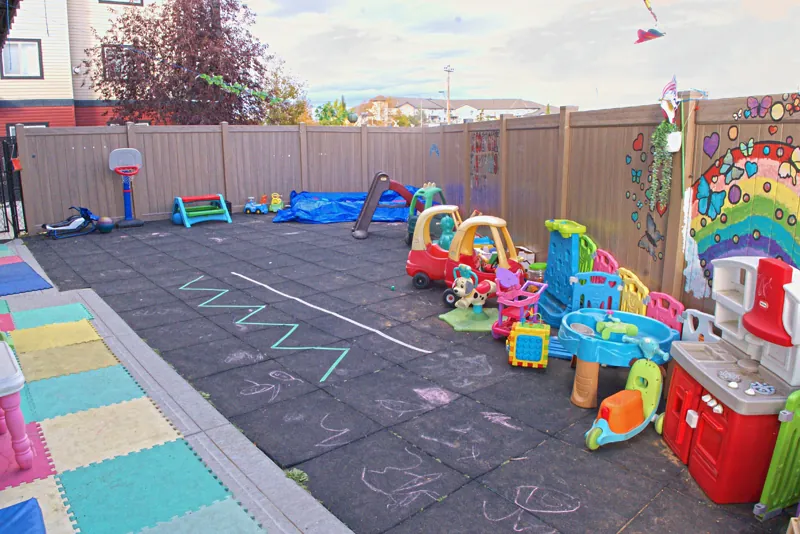 Fenced backyard with ride-on cars, a slide and a painted rainbow mural